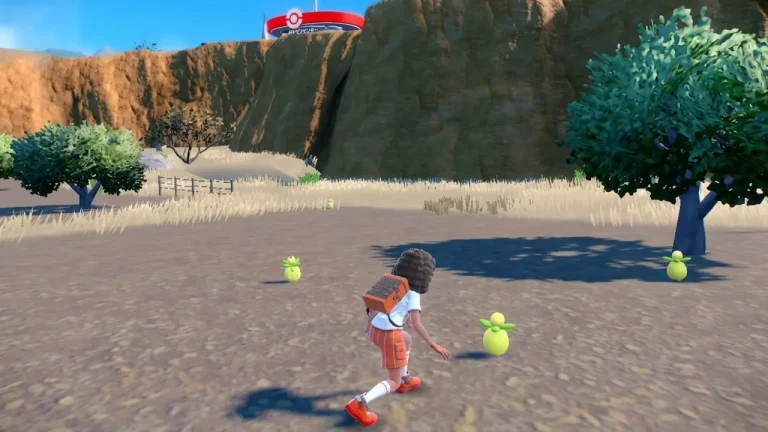 Pokemon Scarlet Switch NSP Trainer crouches to catch small yellow fruit-shaped Pokémon near a Pokémon Center on a sandy trail.